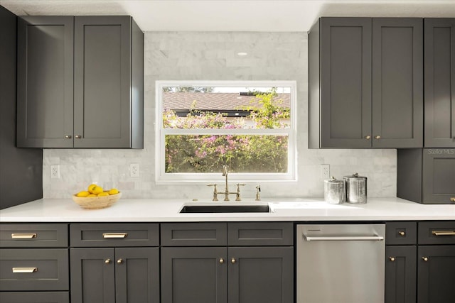 kitchen featuring a sink, light countertops, stainless steel dishwasher, gray cabinets, and tasteful backsplash