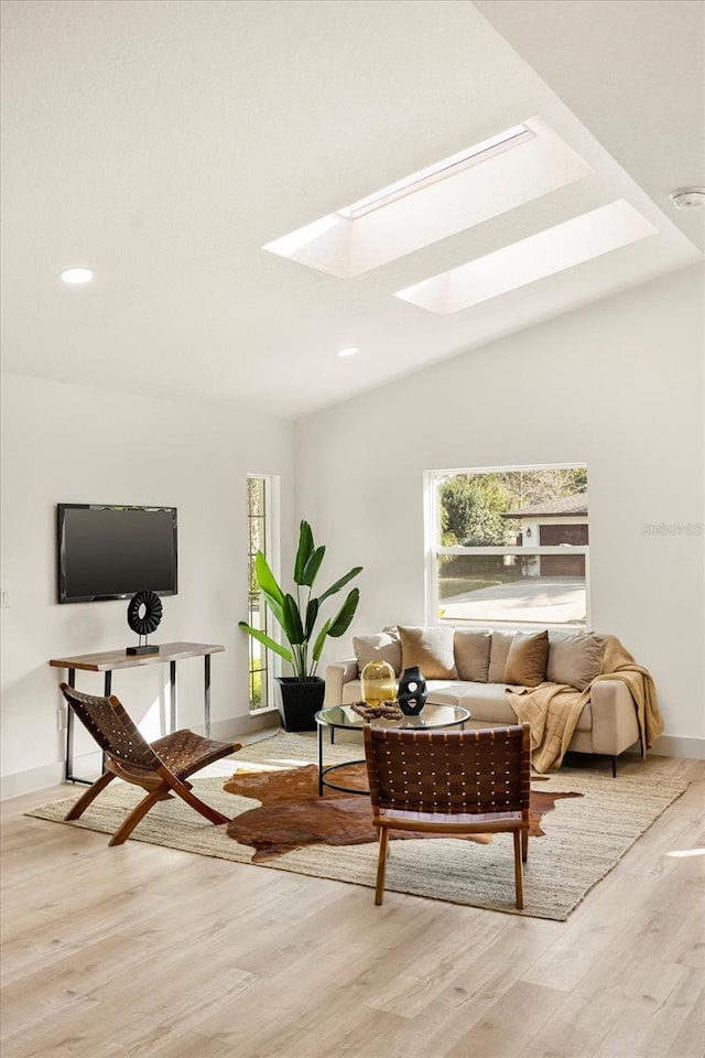 living area with light wood-type flooring, vaulted ceiling with skylight, and recessed lighting