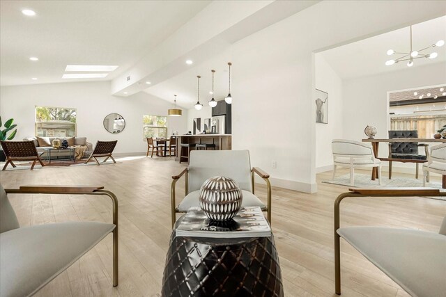 living area with baseboards, lofted ceiling with skylight, a chandelier, and light wood-style floors