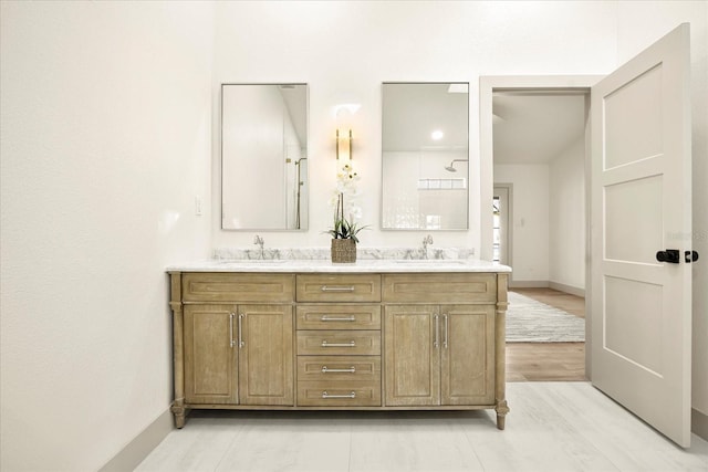 full bathroom with double vanity, wood finished floors, a sink, and baseboards