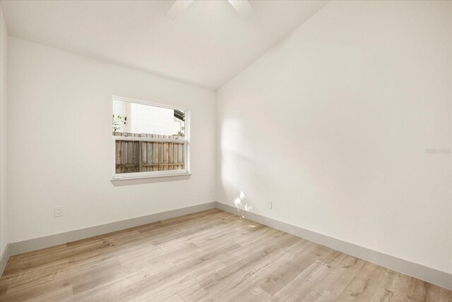 empty room featuring baseboards, vaulted ceiling, and light wood finished floors