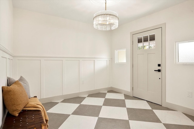 foyer featuring a decorative wall, wainscoting, a chandelier, and light flooring
