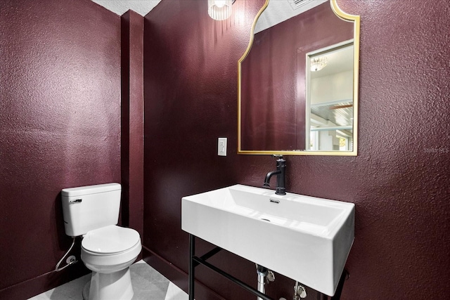 bathroom featuring toilet, a textured wall, a sink, and tile patterned floors