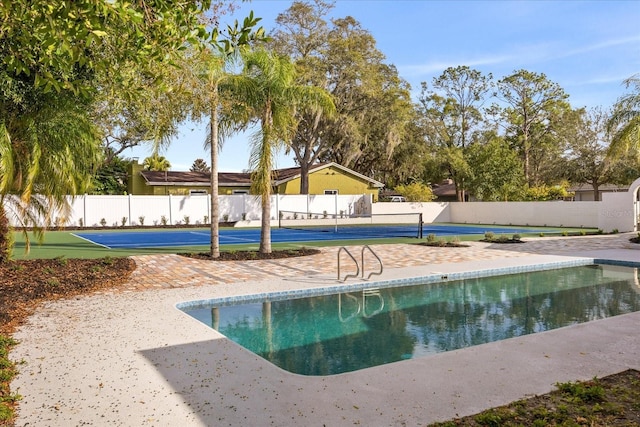 view of swimming pool featuring a tennis court and fence