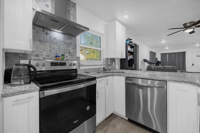 kitchen with sink, stainless steel appliances, wall chimney range hood, light hardwood / wood-style flooring, and white cabinets