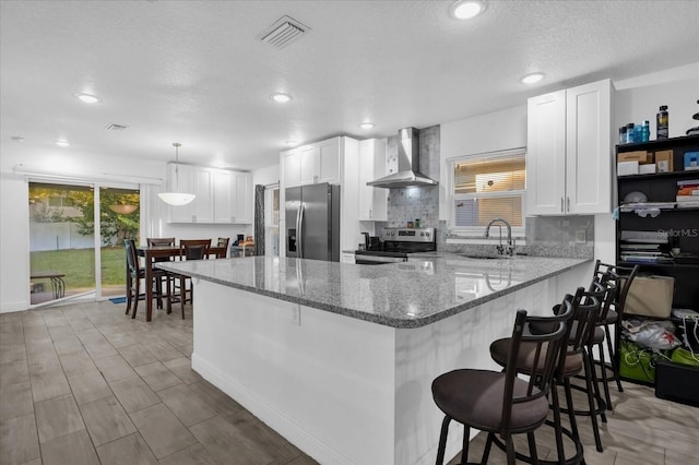 kitchen featuring visible vents, appliances with stainless steel finishes, a peninsula, wall chimney exhaust hood, and a sink