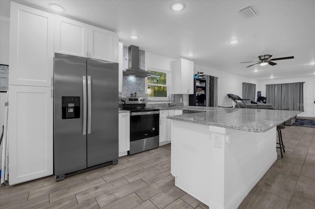 kitchen featuring visible vents, wood finish floors, stainless steel appliances, white cabinets, and wall chimney range hood