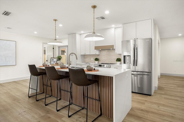 kitchen with sink, white cabinetry, stainless steel appliances, an island with sink, and decorative light fixtures