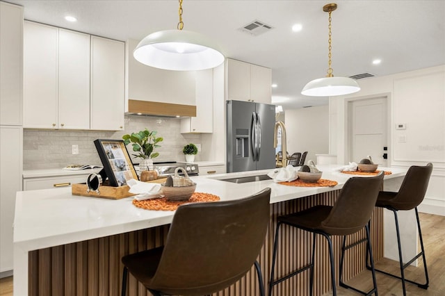 kitchen featuring light hardwood / wood-style flooring, hanging light fixtures, a center island with sink, appliances with stainless steel finishes, and white cabinets