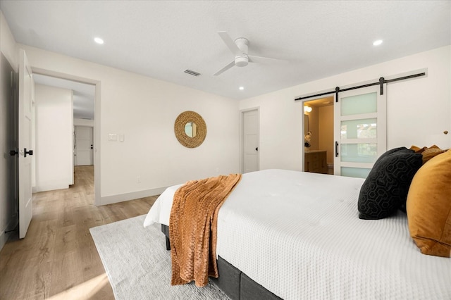 bedroom featuring ensuite bath, light hardwood / wood-style floors, a barn door, and ceiling fan