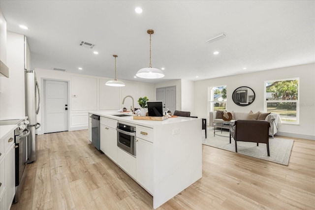 kitchen featuring sink, white cabinetry, hanging light fixtures, stainless steel appliances, and a center island with sink