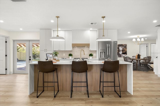 kitchen with custom exhaust hood, white cabinetry, decorative backsplash, and stainless steel fridge with ice dispenser