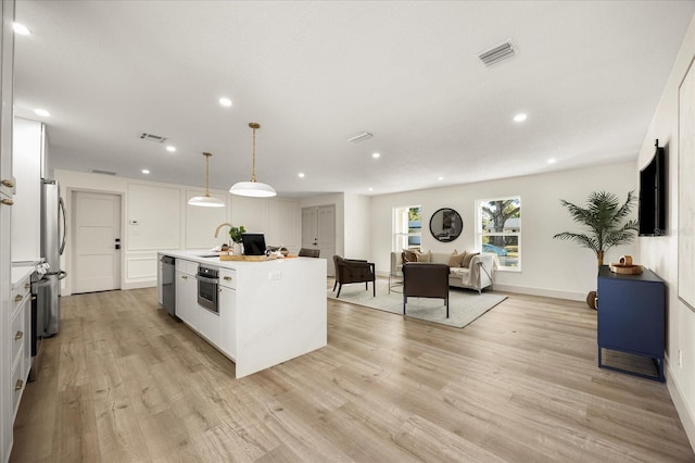 kitchen featuring hanging light fixtures, an island with sink, and white cabinets