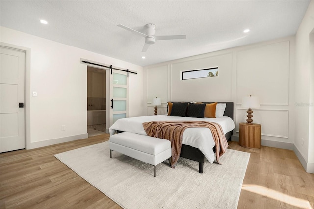 bedroom with ensuite bathroom, a barn door, ceiling fan, and light hardwood / wood-style flooring