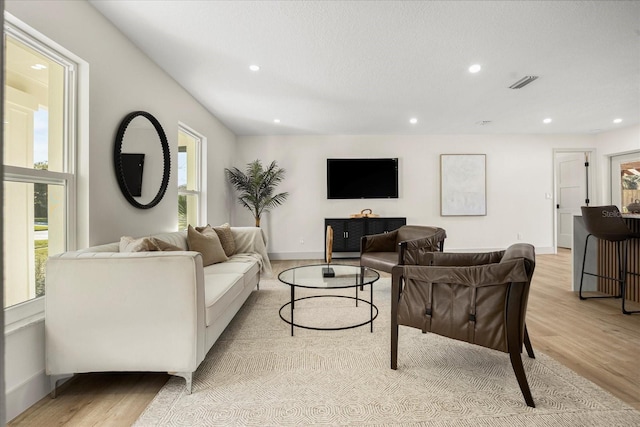 living room featuring visible vents, plenty of natural light, and light wood-style flooring