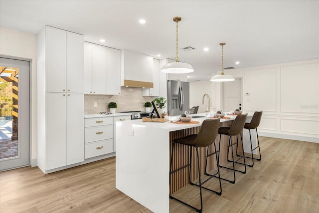 kitchen featuring decorative backsplash, visible vents, a center island with sink, light countertops, and stainless steel appliances