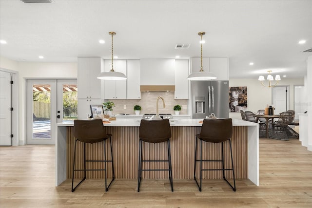 kitchen featuring a large island, visible vents, light countertops, stainless steel fridge, and white cabinetry