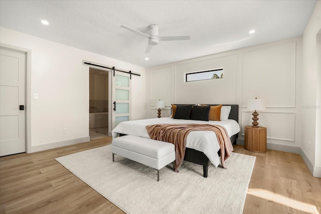 bedroom with light wood-style floors, baseboards, a ceiling fan, and a barn door