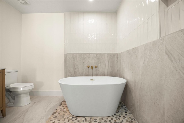 bathroom featuring baseboards, tile walls, toilet, and a soaking tub