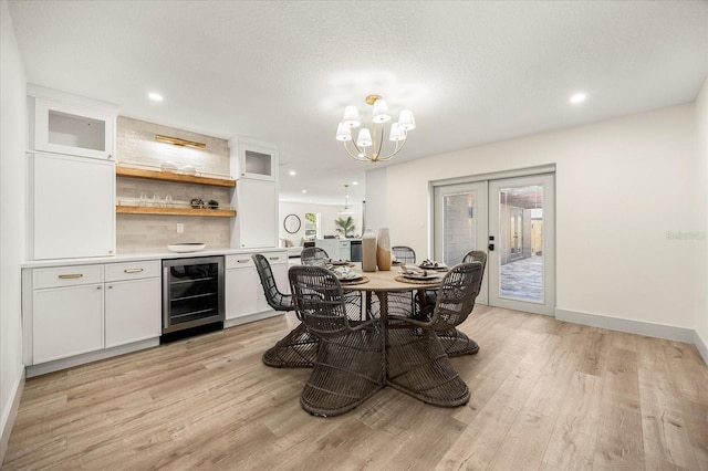 dining space featuring beverage cooler, light wood-style floors, a chandelier, french doors, and a dry bar