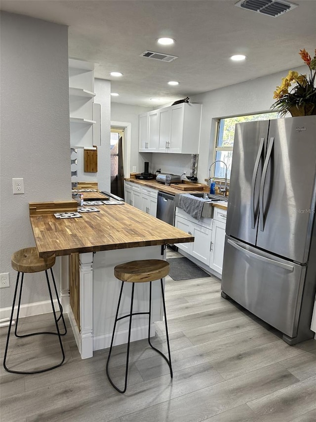 kitchen with stainless steel refrigerator, white cabinetry, butcher block countertops, kitchen peninsula, and a kitchen bar