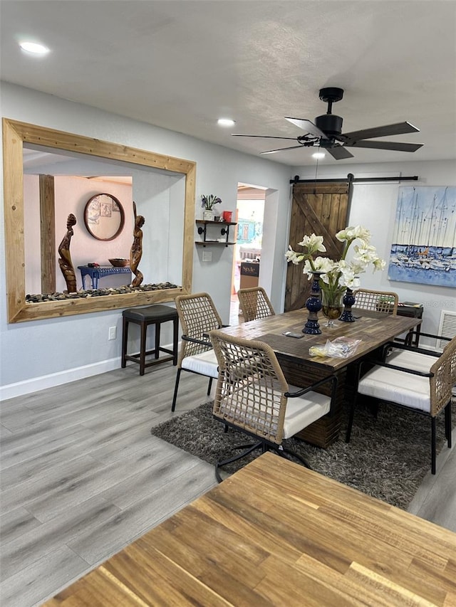 dining area with hardwood / wood-style floors, a barn door, and ceiling fan