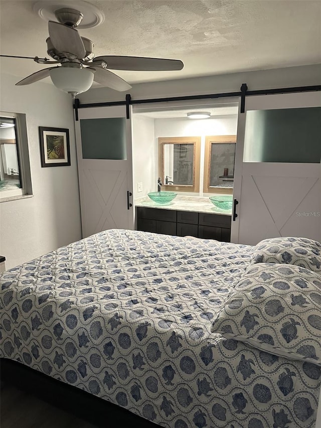 bedroom with ceiling fan, a barn door, and a textured ceiling