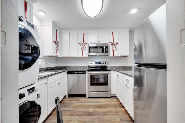 kitchen featuring white cabinetry, sink, light hardwood / wood-style flooring, stacked washer / dryer, and appliances with stainless steel finishes