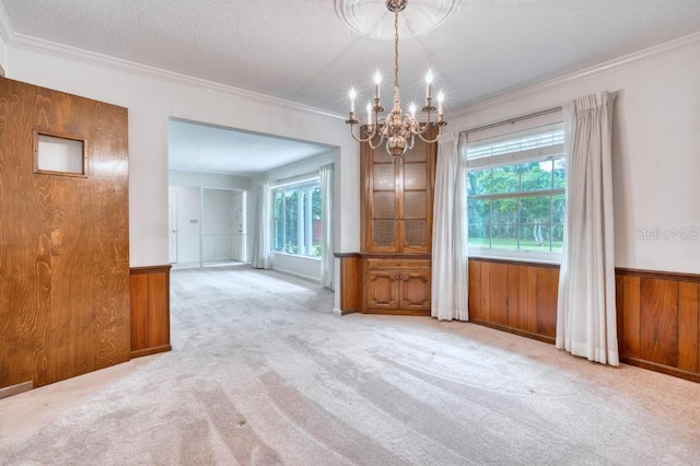 unfurnished dining area with light carpet, ornamental molding, a textured ceiling, wooden walls, and an inviting chandelier