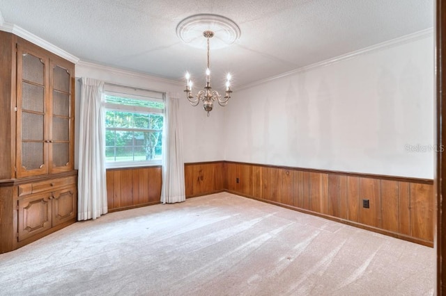 spare room with wood walls, crown molding, light colored carpet, and a notable chandelier