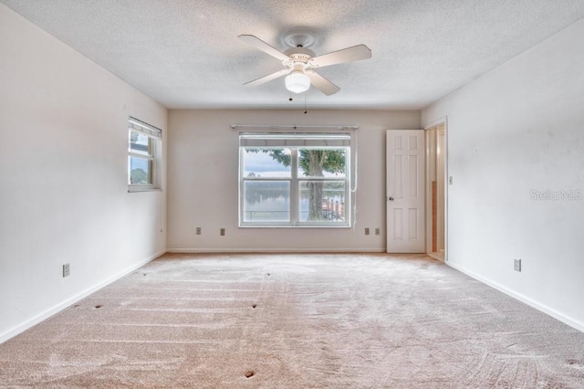 carpeted empty room featuring ceiling fan, plenty of natural light, and a textured ceiling