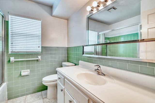 full bathroom featuring combined bath / shower with glass door, vanity, tile walls, tile patterned flooring, and toilet