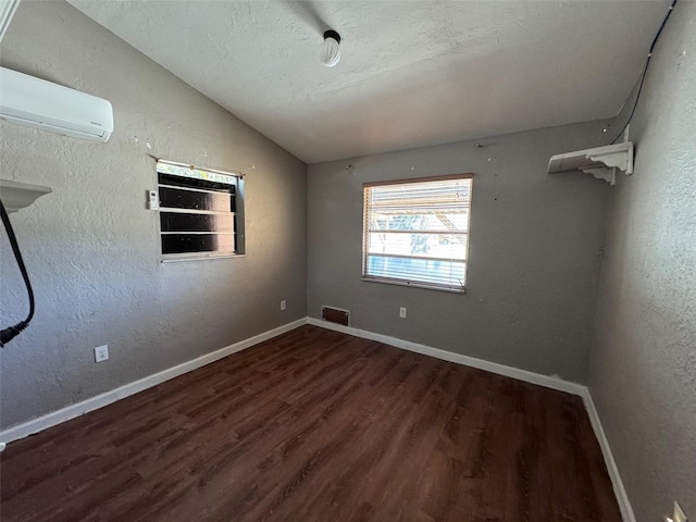 spare room with a wall unit AC, lofted ceiling, a textured ceiling, and dark hardwood / wood-style floors