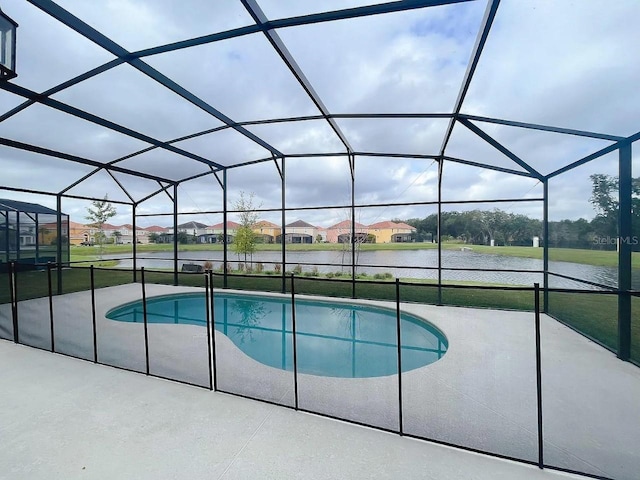 view of pool with a lawn, glass enclosure, a patio area, and a water view