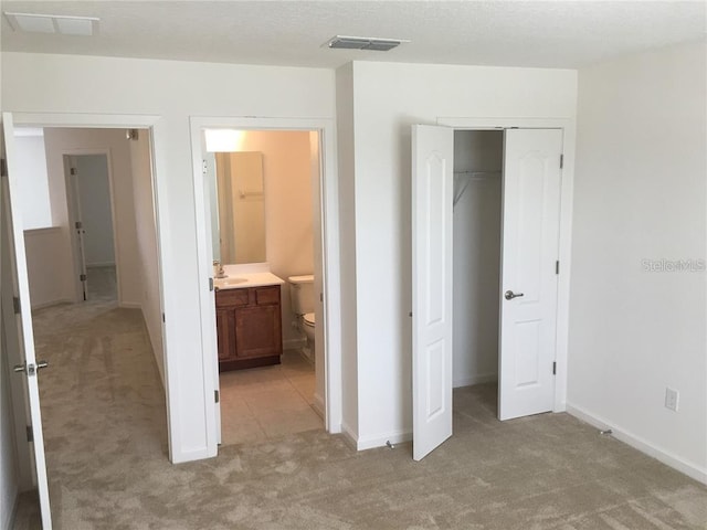 unfurnished bedroom with a closet, sink, light carpet, and ensuite bath