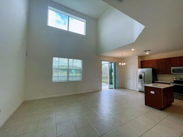 kitchen with light tile patterned floors, a notable chandelier, pendant lighting, a kitchen island, and appliances with stainless steel finishes