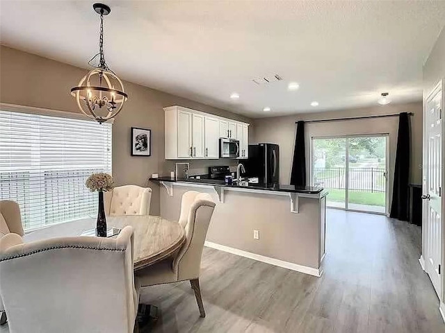 kitchen with black fridge, decorative light fixtures, a notable chandelier, white cabinetry, and a breakfast bar area