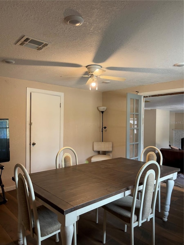 dining area featuring ceiling fan, a textured ceiling, dark hardwood / wood-style flooring, and a fireplace