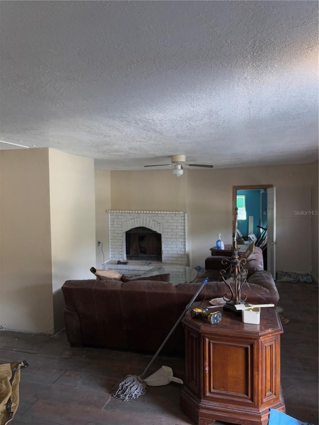 living room featuring a brick fireplace, a textured ceiling, and ceiling fan