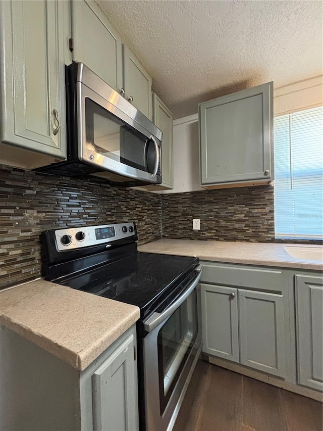 kitchen with a textured ceiling, stainless steel appliances, dark hardwood / wood-style flooring, and tasteful backsplash