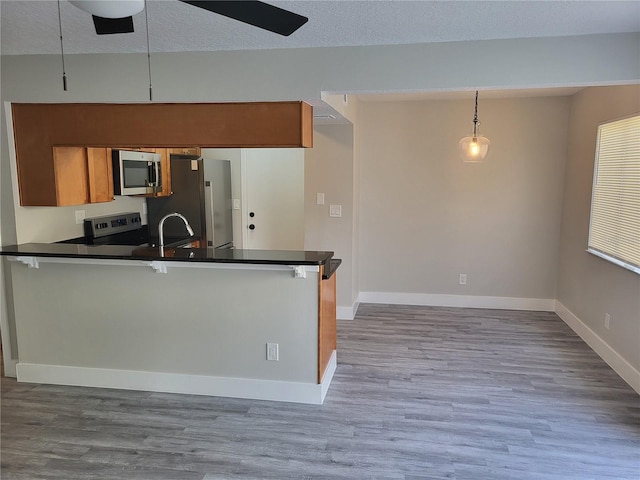 kitchen with kitchen peninsula, pendant lighting, a textured ceiling, a kitchen bar, and appliances with stainless steel finishes