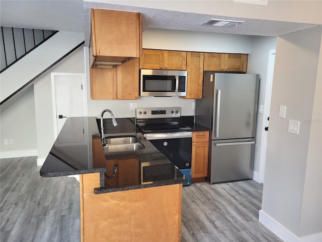 kitchen with a kitchen bar, a textured ceiling, stainless steel appliances, sink, and light hardwood / wood-style flooring