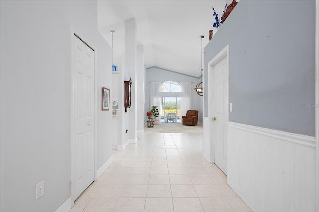 corridor with vaulted ceiling, wainscoting, and light tile patterned flooring