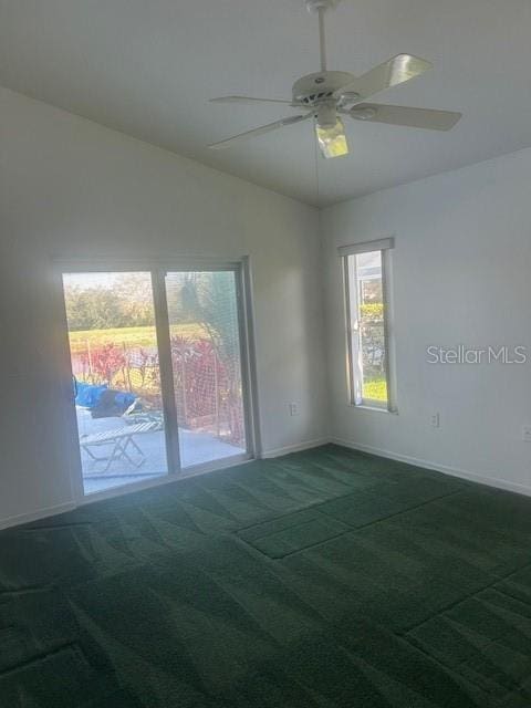 empty room with lofted ceiling, ceiling fan, dark carpet, and baseboards