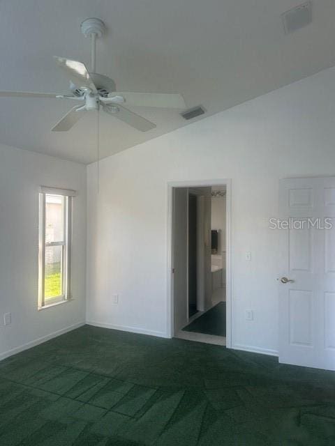 spare room with dark colored carpet, a ceiling fan, visible vents, and baseboards