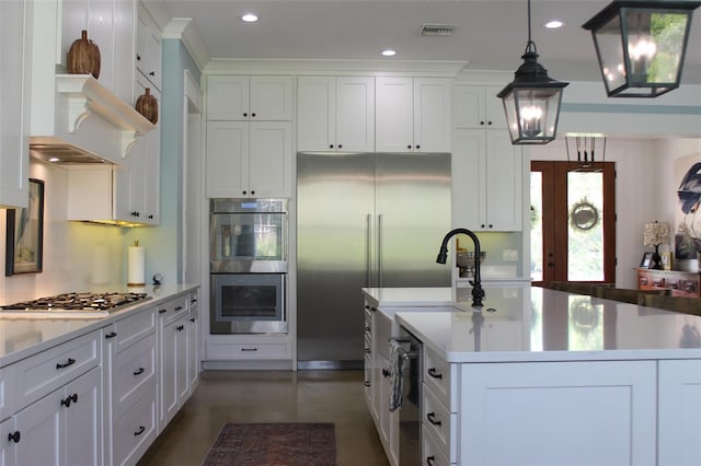 kitchen with white cabinets, decorative light fixtures, a kitchen island with sink, and appliances with stainless steel finishes