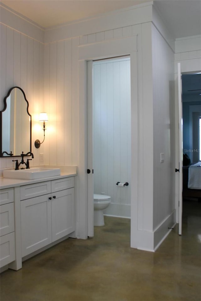 bathroom with concrete flooring, vanity, toilet, and crown molding