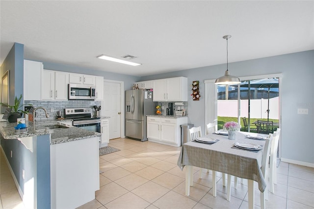 kitchen featuring kitchen peninsula, appliances with stainless steel finishes, light stone counters, decorative light fixtures, and white cabinets