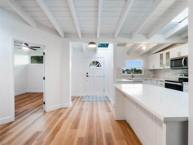 kitchen with white cabinetry, light stone countertops, stainless steel appliances, backsplash, and light wood-type flooring