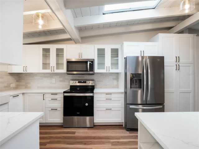 kitchen featuring white cabinetry, hanging light fixtures, backsplash, vaulted ceiling with skylight, and appliances with stainless steel finishes